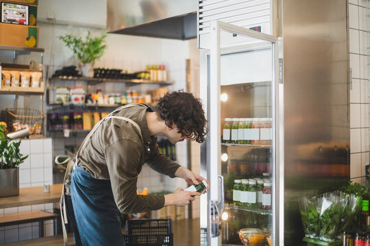 Manlig butiksbitr&auml;de tar flaska fr&aring;n kyl i butik