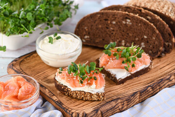 Open sandwich with cheese cream on a slice of rye bread with cereals, slices of marinated salmon, and radish sprouts.