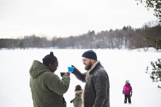 Leende par dricker ur koppar st&aring;ende utomhus med barn