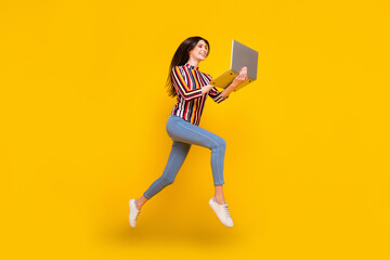 Fototapeta na wymiar Full length body size photo girl in casual clothes jumping working on computer isolated bright yellow color background