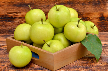 box with green apples on wooden background