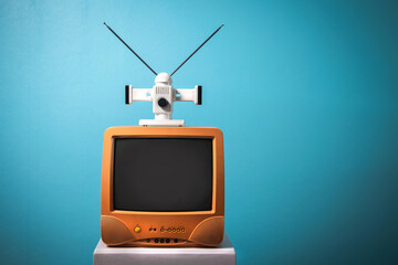 Yellow TV color, retro CRT television receivers with antenna on white wooden box with mint blue background.