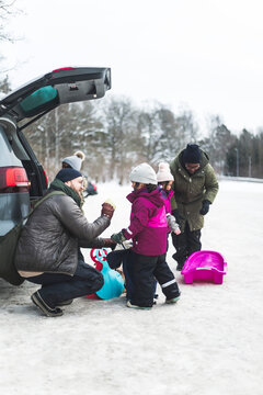 Pappa pratar med d&ouml;ttrar sittande p&aring; huk vid bil utomhus