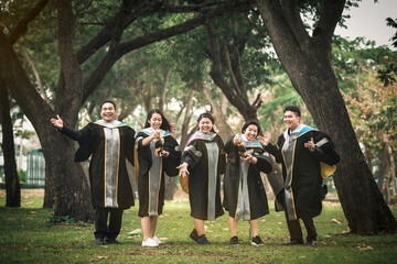 A group of college students celebrate graduation with champagne in the open air among the trees.