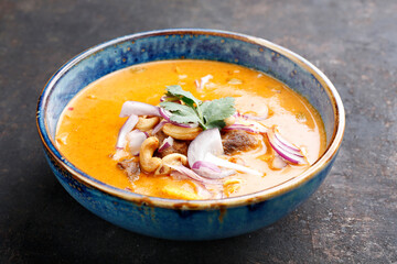 A close-up of massaman curry in an oriental bowl on black stony background. Thai curry based on cashew nut paste, cardamom, cinnamon and coconut milk with pieces of lamb meat and tofu. Fusion cousine.