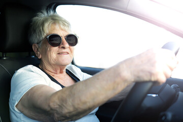 Happy senior woman in sunglasses driving automobile.