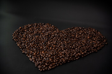 Freshly roasted coffee beans. It is a heart shape placed on a black background.