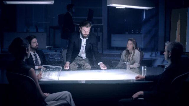 In the Near Future: Businessman in Suit presenting Architecture Project to Colleagues and Partners sitting around Futuristic Table with Holographic Modern Augmented Reality Technology.