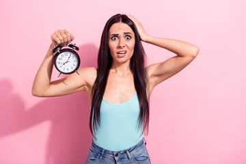 Portrait of attractive worried funky long-haired girl holding clock oops isolated over pink pastel color background