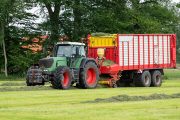 Fototapeta na wymiar Picking up dried grass for silage with a green tractor and red loader wagon.