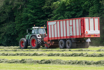 Picking up dried grass for silage with a green tractor and red loader wagon.