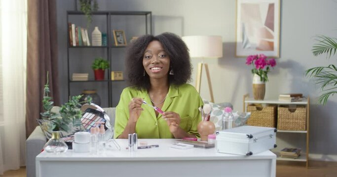 Makeup female vlogger creating cosmetic product explainer video. Portrait of African American woman recording personal make up vlog video. Young happy pretty influencer beauty fashion blogger