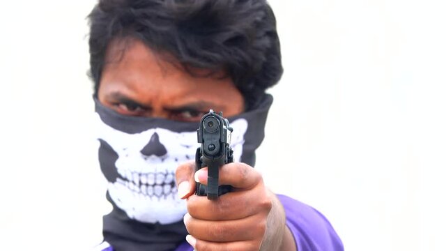 man with gun aiming towards the camera with left hand wearing a skull mask covering his face 