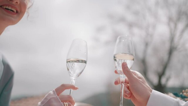 Close up side view of groom and bride hands clinking glasses with wine during their wedding. Action. Concept of celebration and starting family.