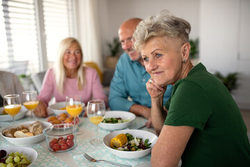 Senior woman with friends having party indoors, eating at the table.