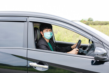 Fototapeta na wymiar A man wearing a work suit drives a sedan to work in the city. wearing a medical mask to prevent infection during the coronavirus epidemic The driver of the sedan wears a mask for Covid-19.