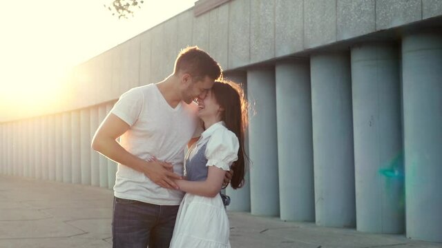 Beautiful happy young people kiss each other, having fun, embracing and enjoying summer time together outside. Portrait of cheerful romatic couple of young man and woman kissing outdoors at sunset.