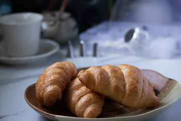 croissant on a brown plate next to a mug of milk on marble background