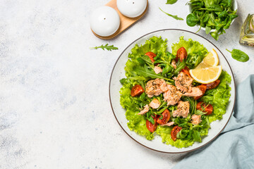 Salad with baked salmon fish. Green salad mix with tomatoes anf salmon. Top view at white table.
