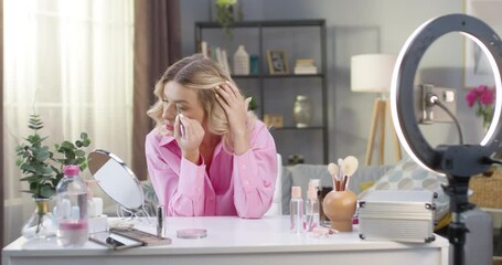 Portrait of modern Caucasian pretty female beauty blogger filming makeup tutorial video on smartphone camera in home studio using cosmetic product. Joyful young woman vlogger speaking in vlog video