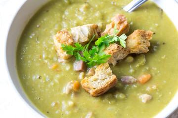 Delicious yummy pea and ham soup with croutons - close up top view image on white