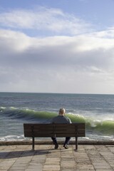 old man looking at the sea sitting on a bench