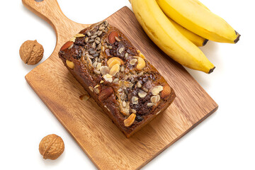 Banana cake topped with almonds is placed on a wooden tray with bananas on the side on a white...