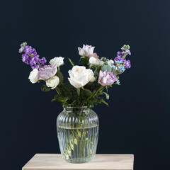 Bouquet of hackelia velutina, purple and white roses, small tea roses, matthiola incana, blue iris in glass vase opposite on black background.