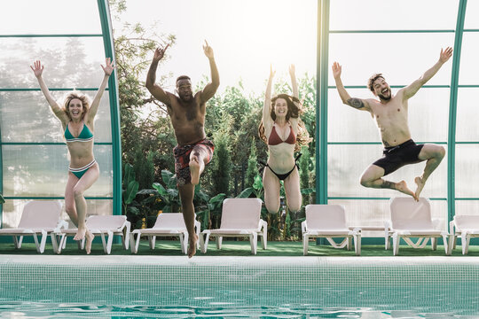 Multiracial people having fun at indoor pool party while jumping in the water - Luxury villa hotel summer lifestyle with friends concept - Focus on african american man face