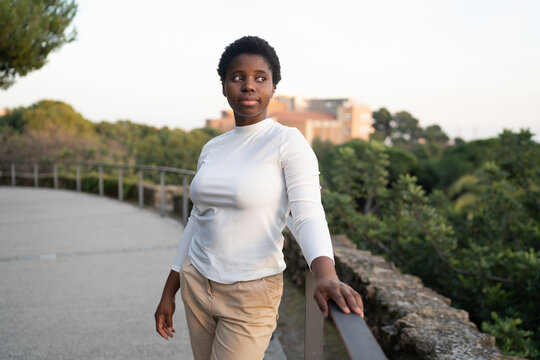 Positive black woman standing near railing in summer park