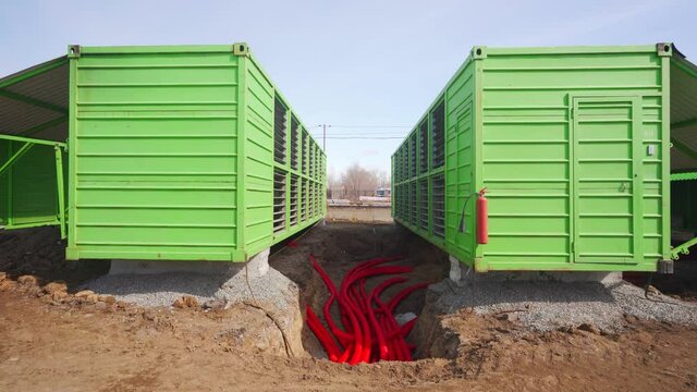 Modular bitcoin mining farm construction site. ASIC mining equipment in green steel shipping containers. Installing powerful server blockchain datacenter. Electrical power cables in trench.
