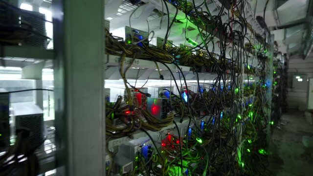 Bitcoin miners in large farm. ASIC mining equipment on stand racks mine cryptocurrency in steel container. Blockchain techology application specific integrated circuit datacenter. Server room lights.