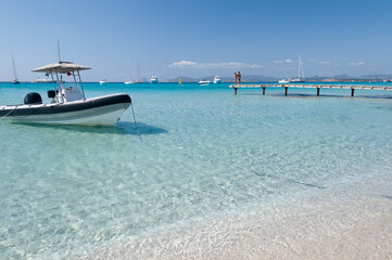 Fototapeta premium A zodiac on the beach of Illetas, the island of Formentera in Spain. In the background the blue sky and a wooden pier with tourists. 