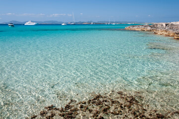 Panoramic view of the coast of Espalmador island of Formentera, Spain. In the background luxurious anchored boats and the blue sky