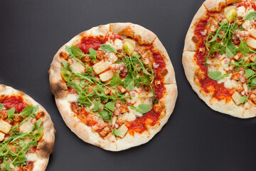 Three Pizzas with smoked ham and rucola on black background. Top view. Tasty pizza with meat on dark ground
