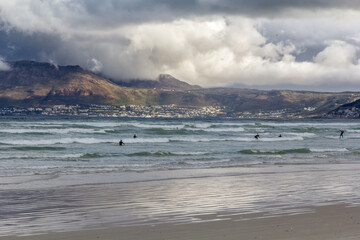 Oleaje intenso en la playa de Muizenberg (Ciudad del Cabo, Cabo de Buena Esperanza, Sud África) en un atardecer con nubes y viento de invierno. Los surfistas aprovechan las olas frente a las montañas 