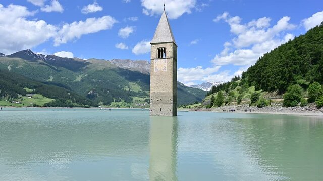Curon, Italy, June 2021. Amazing pan footage on a beautiful summer day of the old bell tower of Curon (Graun) emerging from the waters of Lake Resia, South Tyrol, Italy.