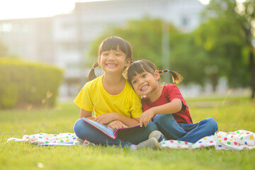 Fototapeta premium Smiling little asian girl happy small sitting on nature in the park. Which increases the development and enhances outside the classroom learning skills concept.
