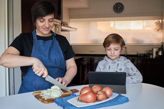Cheerful boy using tablet near cooking mother