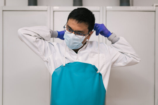 Ethnic doctor putting on protective apron in clinic