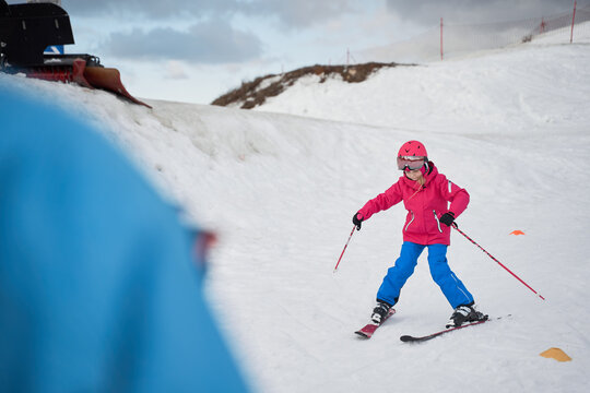 Unrecognizable parent and kid skiing on snowy hill slope