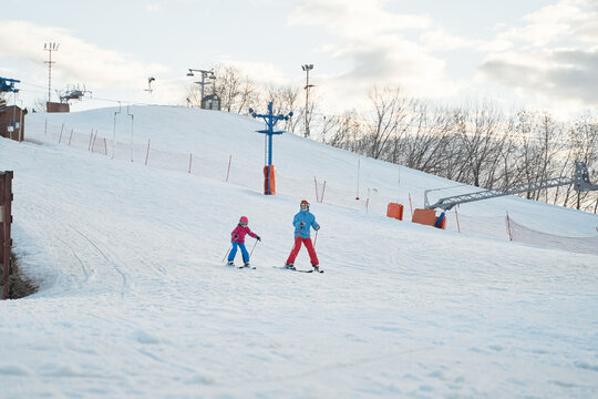 Unrecognizable parent and kid skiing on snowy hill slope