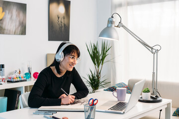Woman drawing in notepad and watching tutorial on laptop