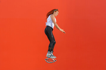Latin redhead mature fit slim woman in kangoo jumps boots training on orange background. Active movement, action, fitness and wellness