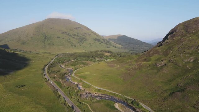 Aerial scenic view of Glencoe, Scotland, UK. Drone view of new road and old single lane road with surrounding high hills on sunny summer day