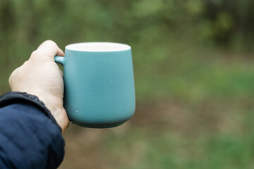 Cup in a man's hand against a background of green forest.