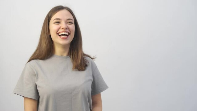 A beautiful young girl in a gray T-shirt and with long hair tells something to the camera