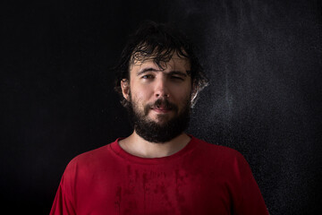 Portrait of a young dark-haired man with a beard with wet hair on a dark background with water drops