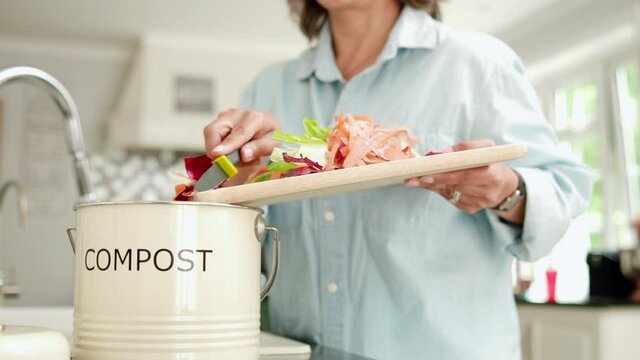 Close Up Of Woman In Kitchen Making Compost Scraping Vegetable Leftovers Into Bin