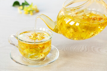 Herbal tea from lime blossoms is poured from the kettle into the cup. The concept of alternative medicine
